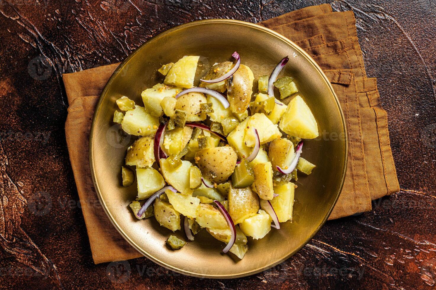 Warm Potato salad with red onion, capers, greens in a plate. Dark background. Top view photo