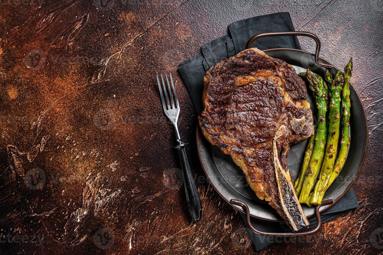 BBQ Grilled Tomahawk or Cowboy with bone beef steak, roasted asparagus. Wooden background. Top view. Copy space photo