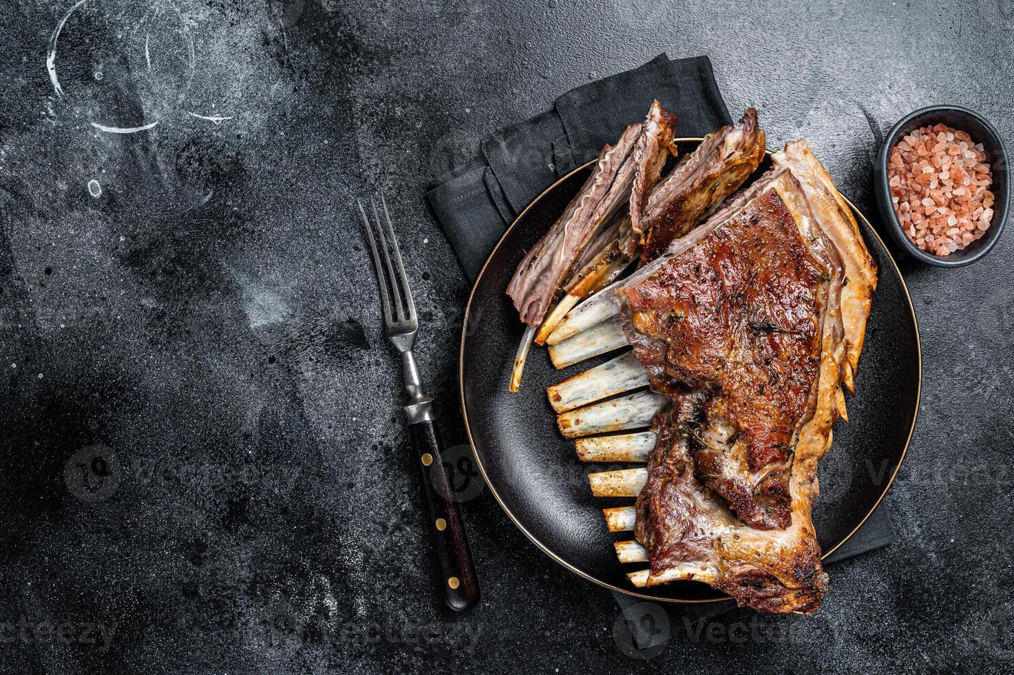 Roasted Rack of lamb ribs, mutton spareribs, sliced meat on plate. Black background. Top view. Copy space photo