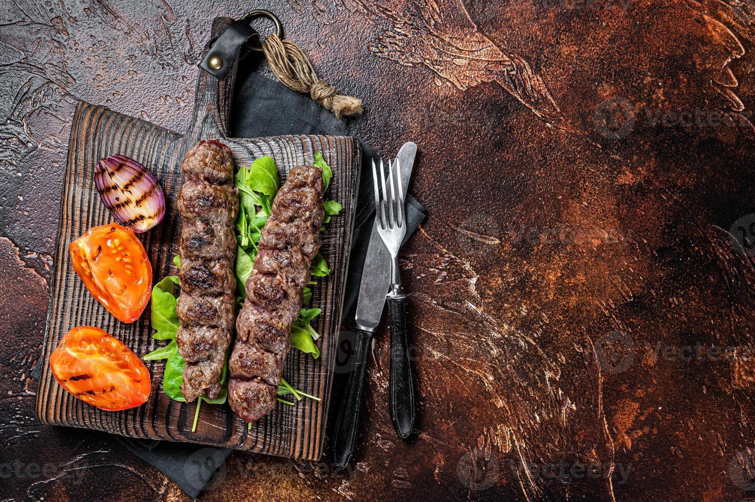 Turkish adana kebab, ground beef and lamb meat grilled on skewers served with tomato, salad and onion. Dark background. Top view. Copy space photo