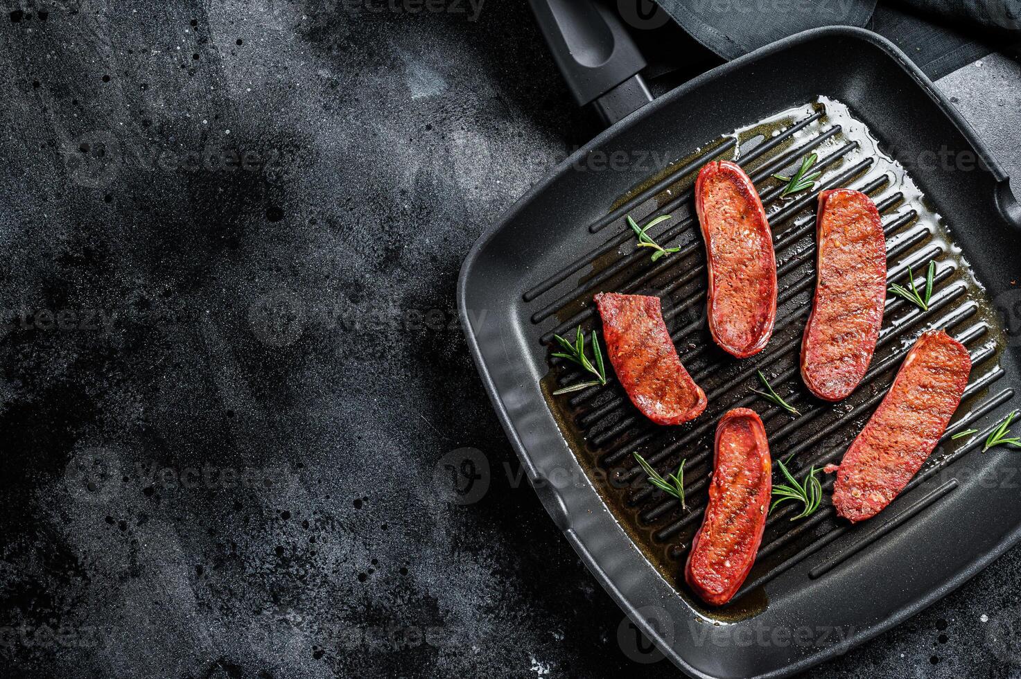 Fried Turkish Sucuk meat sausage on a grill skillet. Black background. Top view. Copy space photo