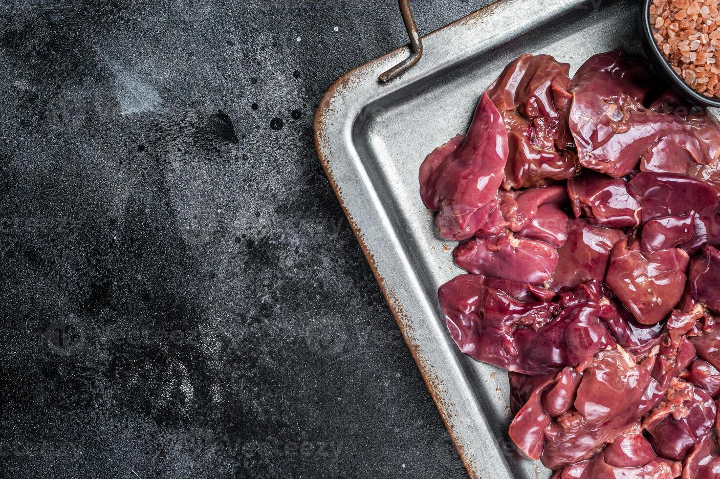 Raw chicken liver meat in steel tray with spices. Black background. Top view. Copy space photo