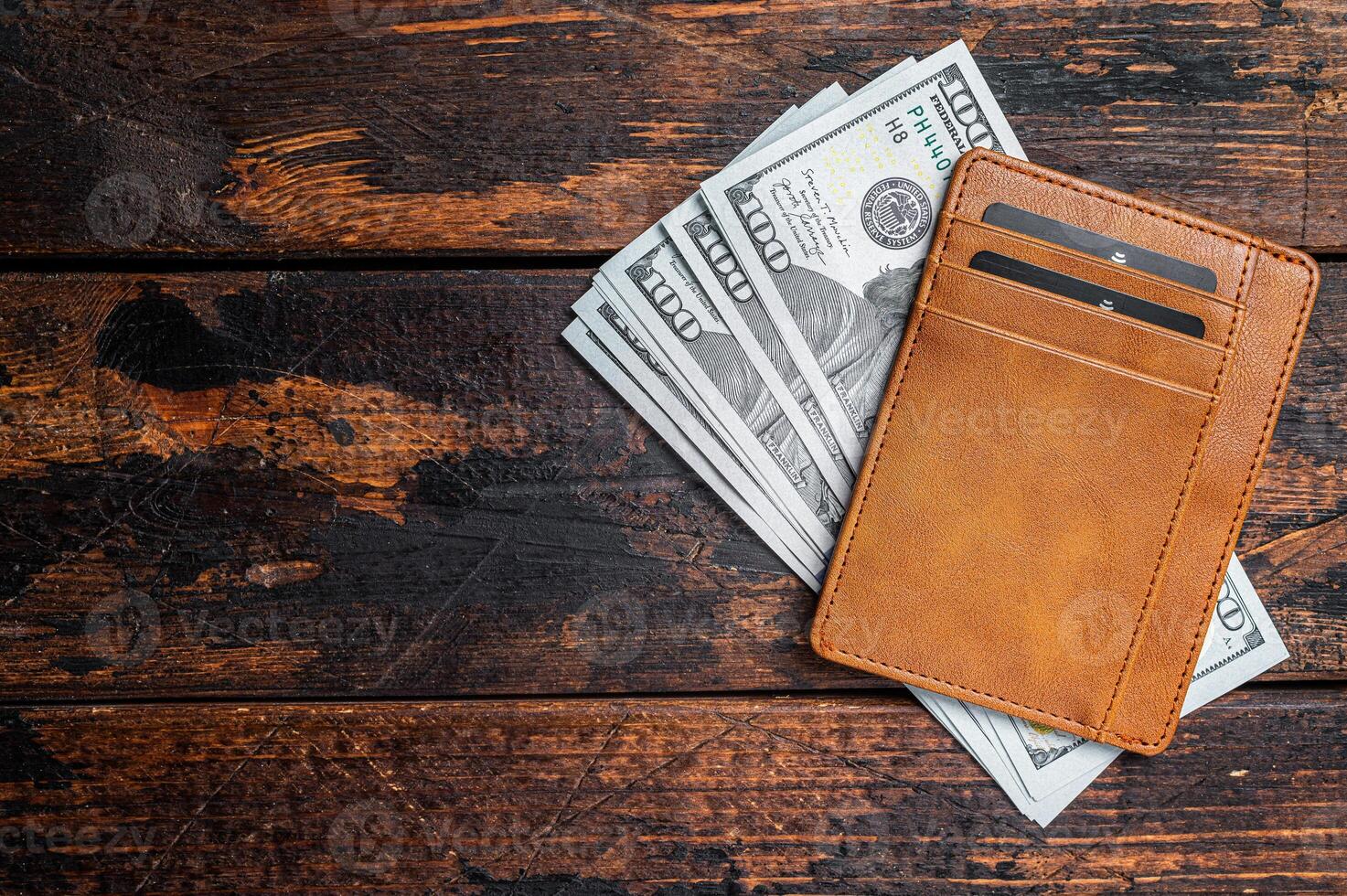 One hundred dollar bill in a brown leather wallet with credit cards. Brown background. Top view. Copy space photo