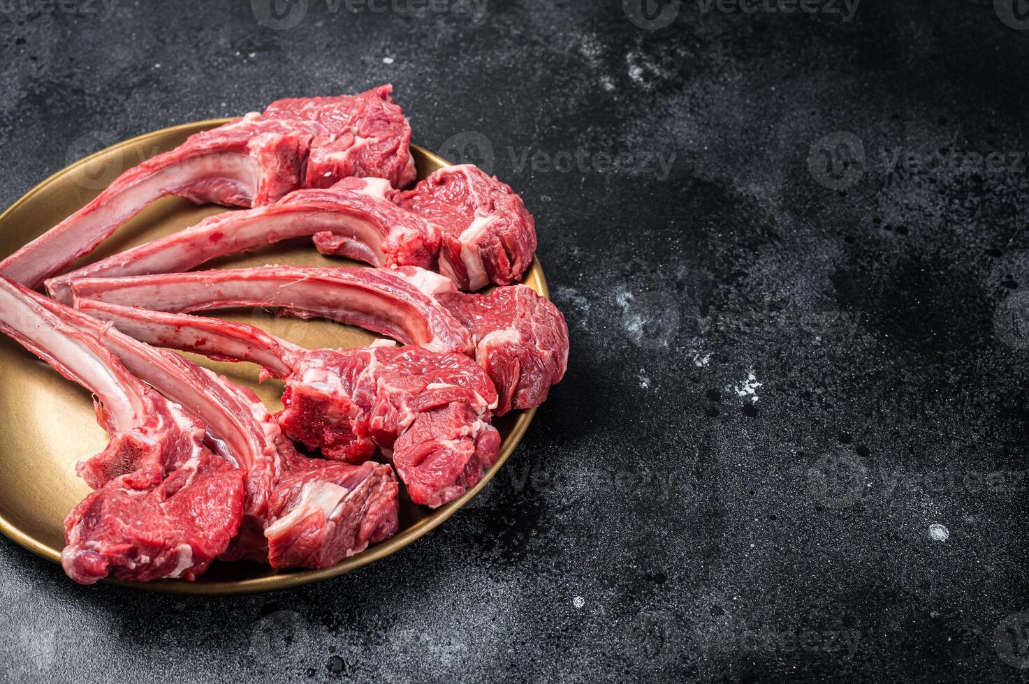 Lamb chop rib steak, raw mutton meat cutlet in golden plate. Black background. Top view. Copy space photo