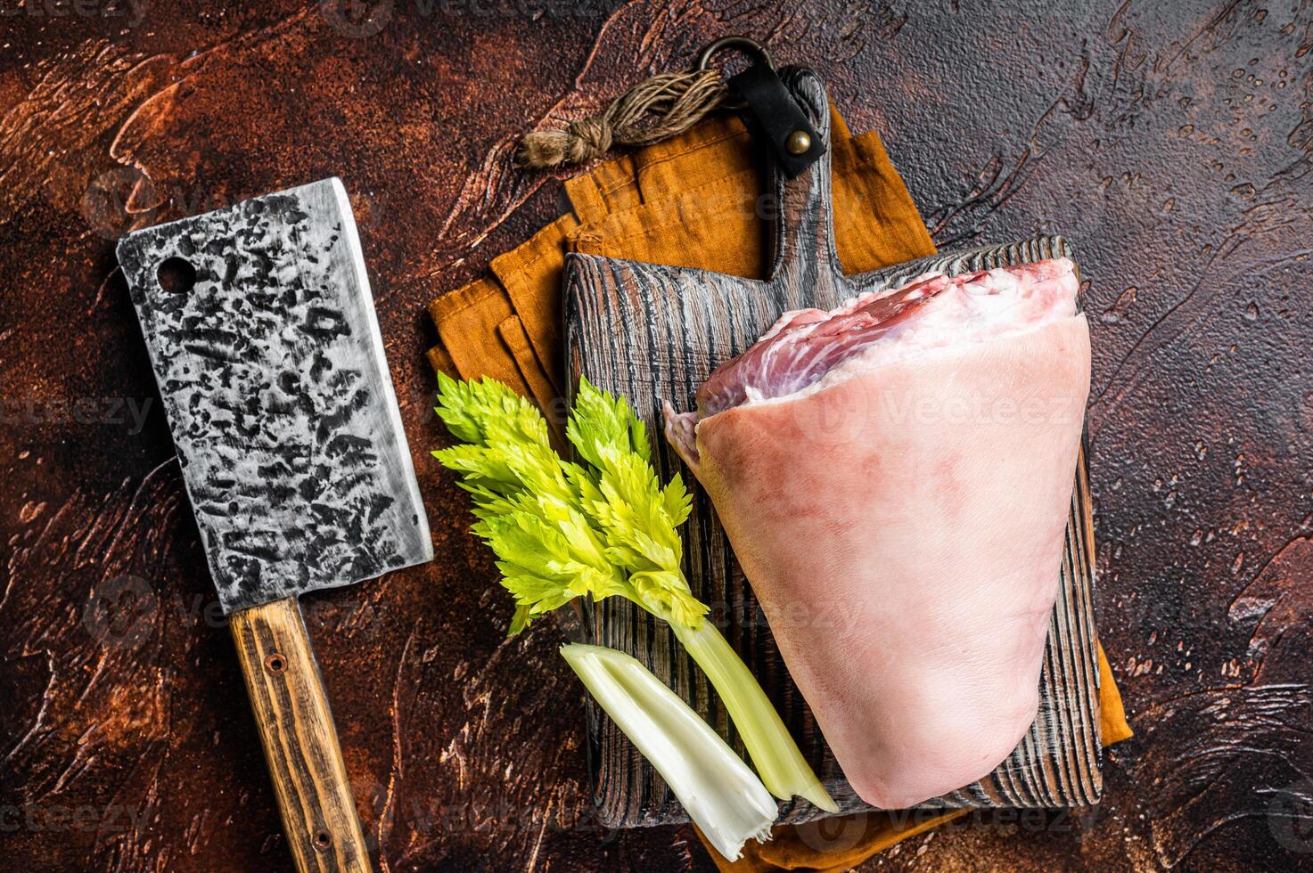 Fresh Raw pork shank knuckle on a butcher board with herbs for cooking. Dark background. Top view photo