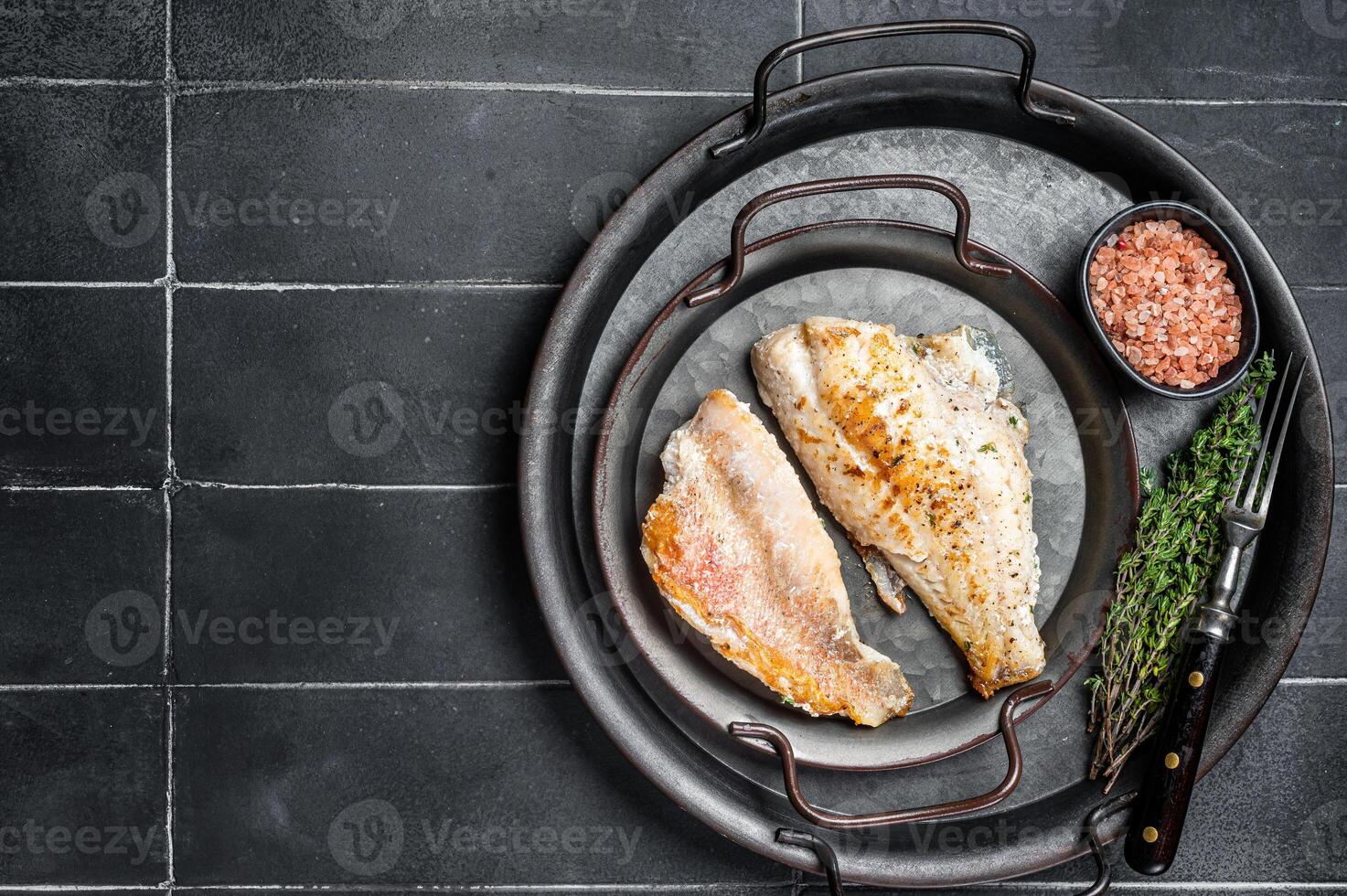 Roasted ocean red perch fillet with olive oil, thyme and spices. Black background. Top view. Copy space photo
