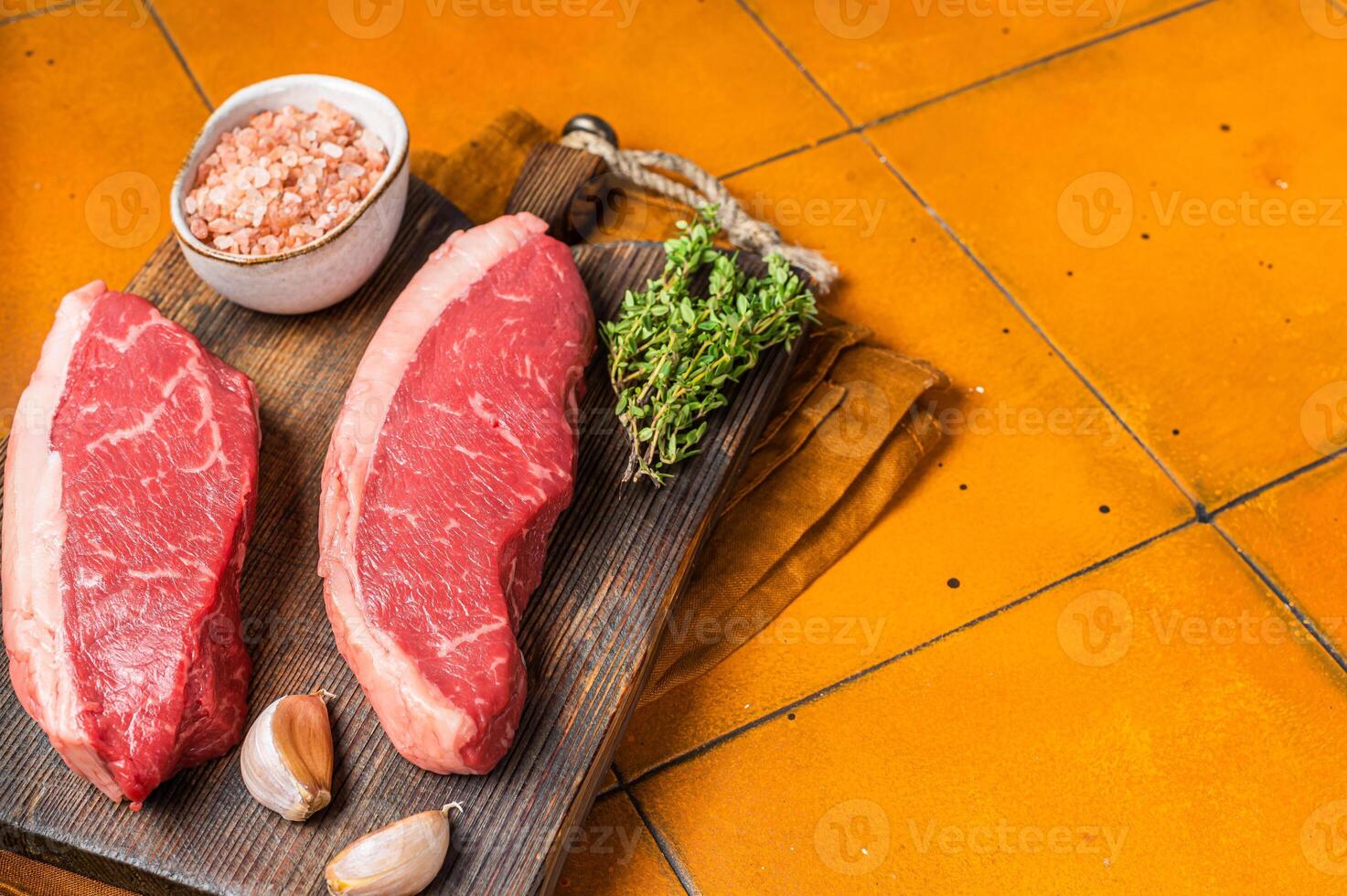 Cap Rump steak, raw beef meat steak with thyme and salt on wooden butcher board. Orange background. Top view. Copy space photo