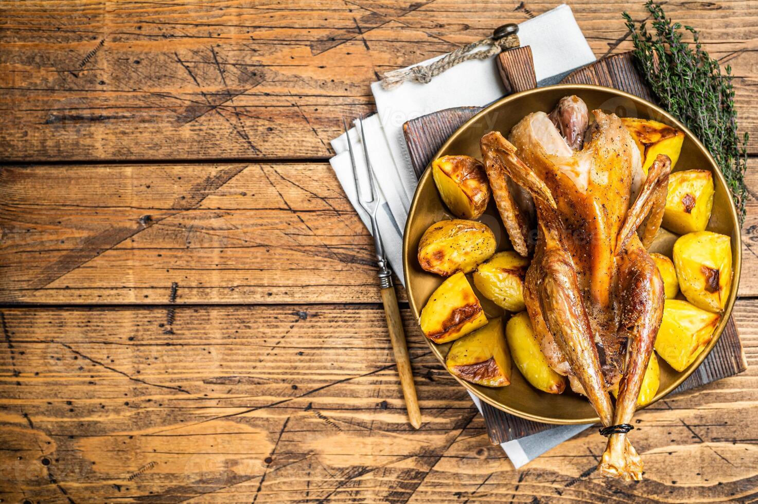Roasted guinea fowl with herbs and potato, cooked farm eco bird. Wooden background. Top view. Copy space photo
