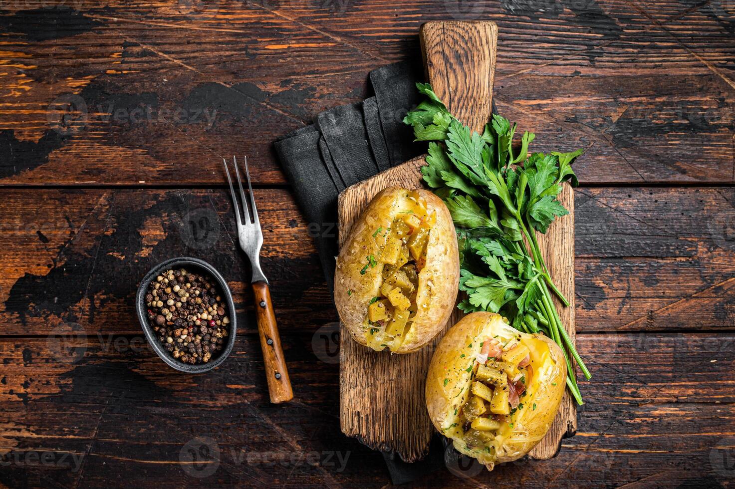 Kumpir, baked Jacket potatoes stuffed with cheese, bacon, salty cucumber, herbs and butter. Wooden background. Top view photo