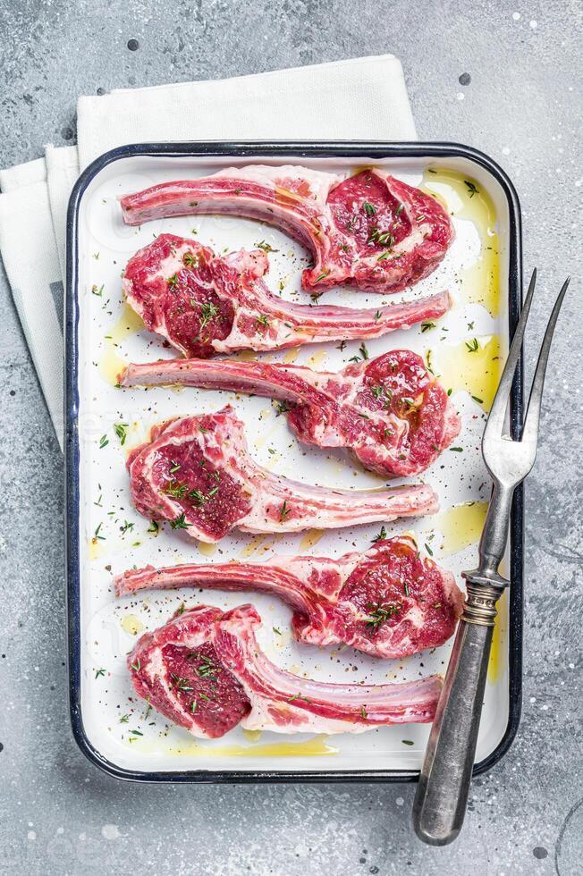 Ready for cooking raw lamb chop steaks with spices and herbs. Gray background. Top view photo