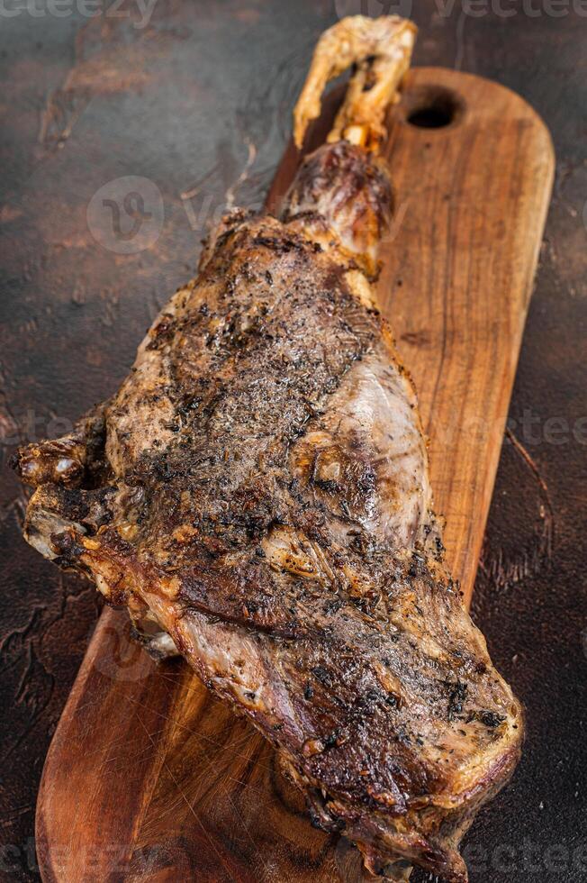 Roast lamb leg meat with herbs and spices on a cutting board. Dark background. Top view photo