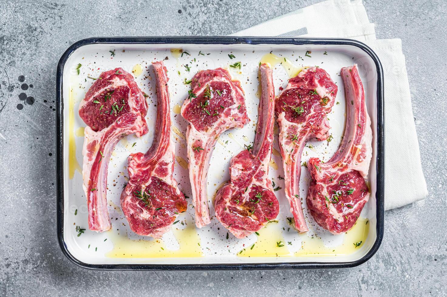Ready for cooking raw lamb chop steaks with spices and herbs. Gray background. Top view photo