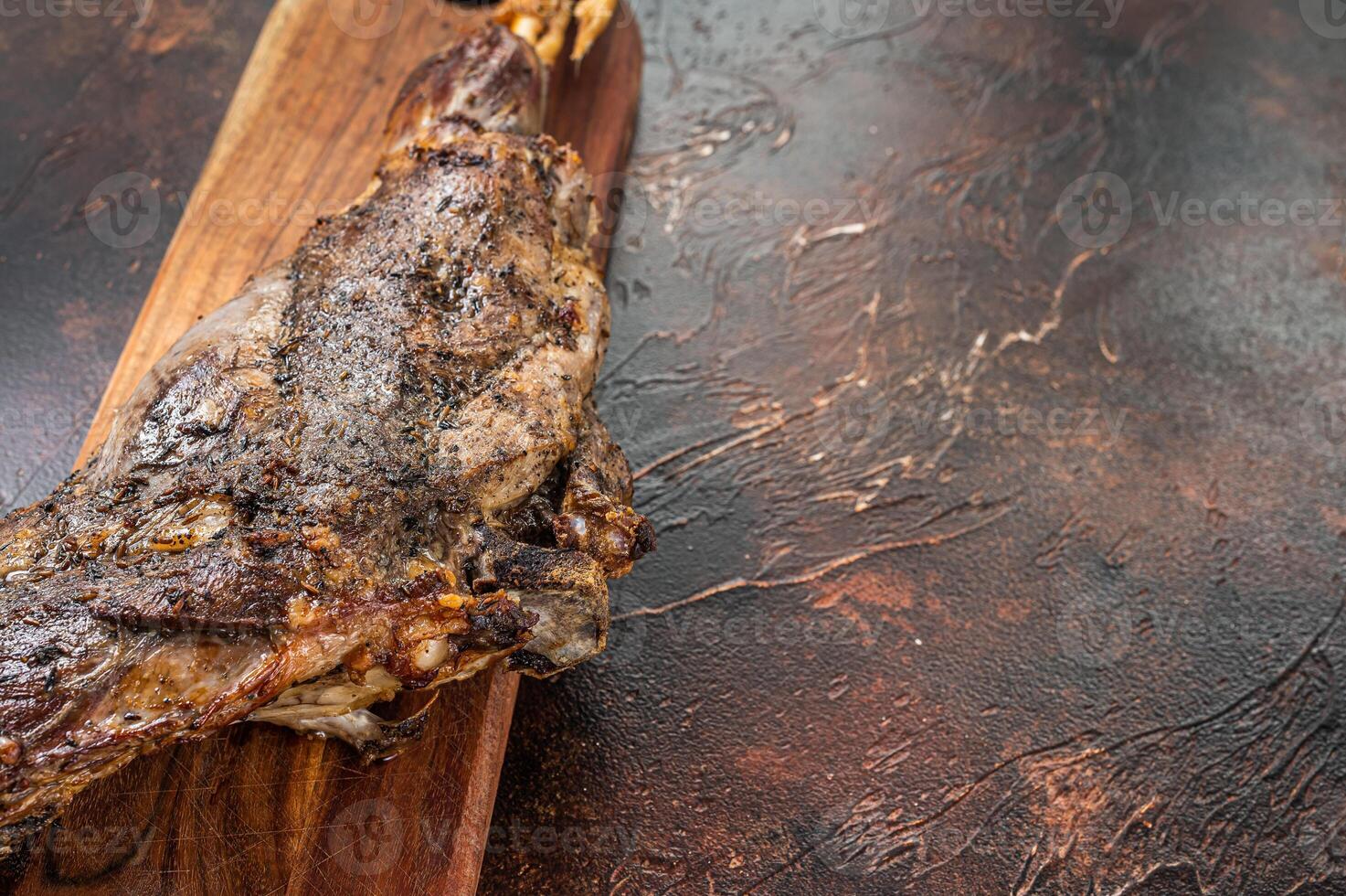 Roast lamb leg meat with herbs and spices on a cutting board. Dark background. Top view. Copy space photo