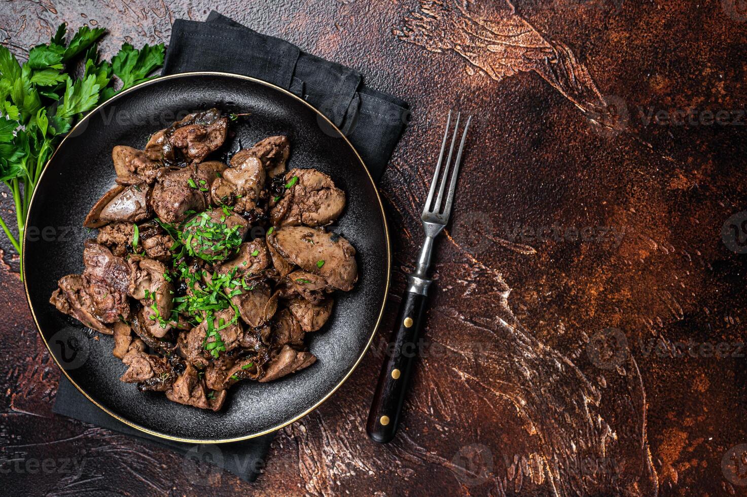 Fried chicken liver with onions and parsley in a plate. Dark background. Top view. Copy space photo