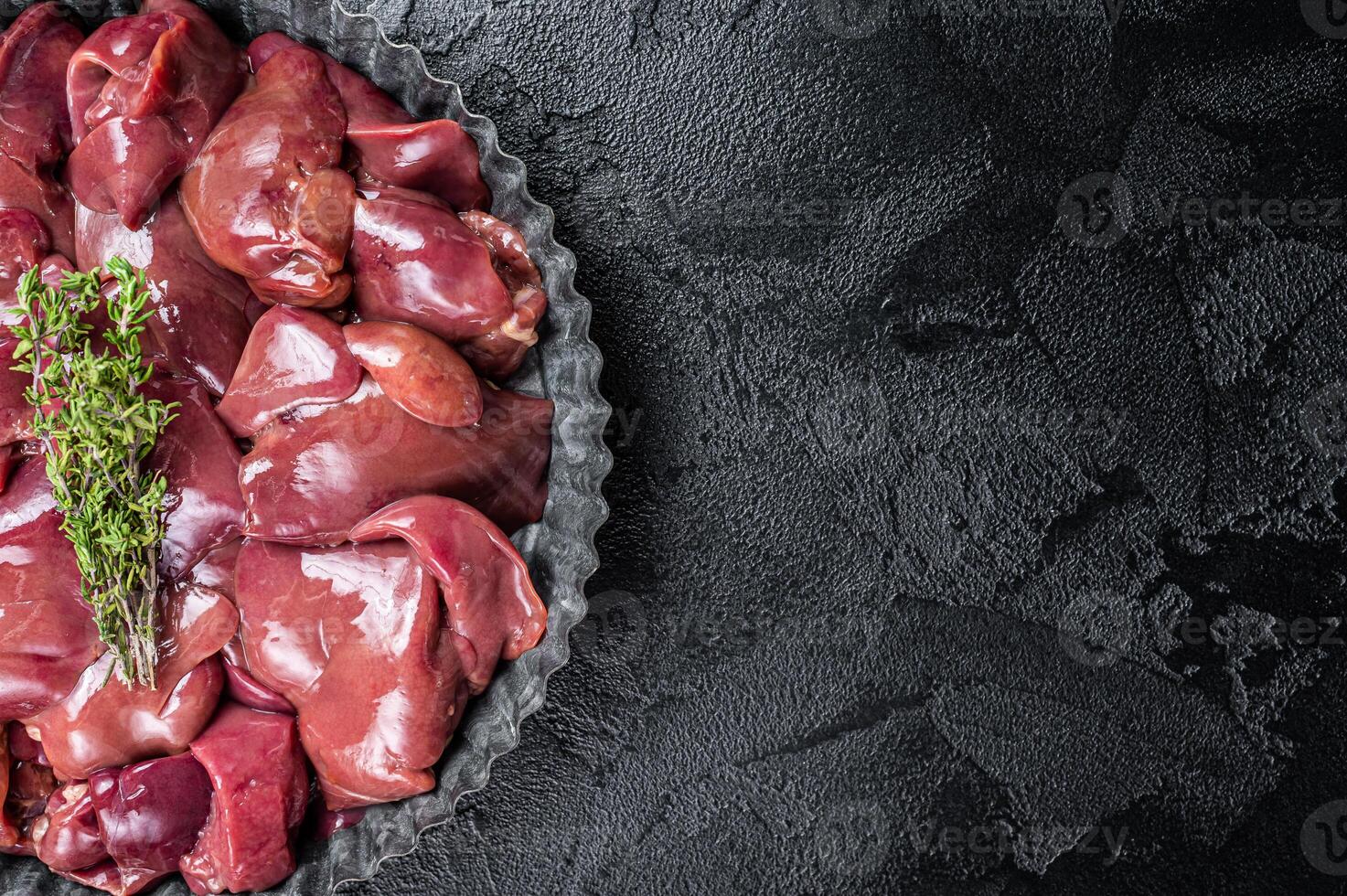 Uncooked Raw chicken liver, poultry offals in steel plate. Black background. Top view. Copy space photo