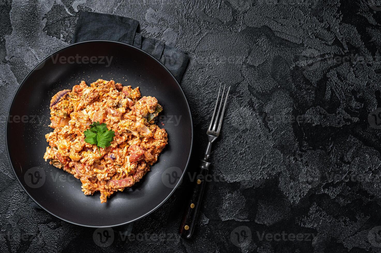 Turkish Menemen, Eggs with tomatoes, green peppers and green onion. Black background. Top view. Copy space photo