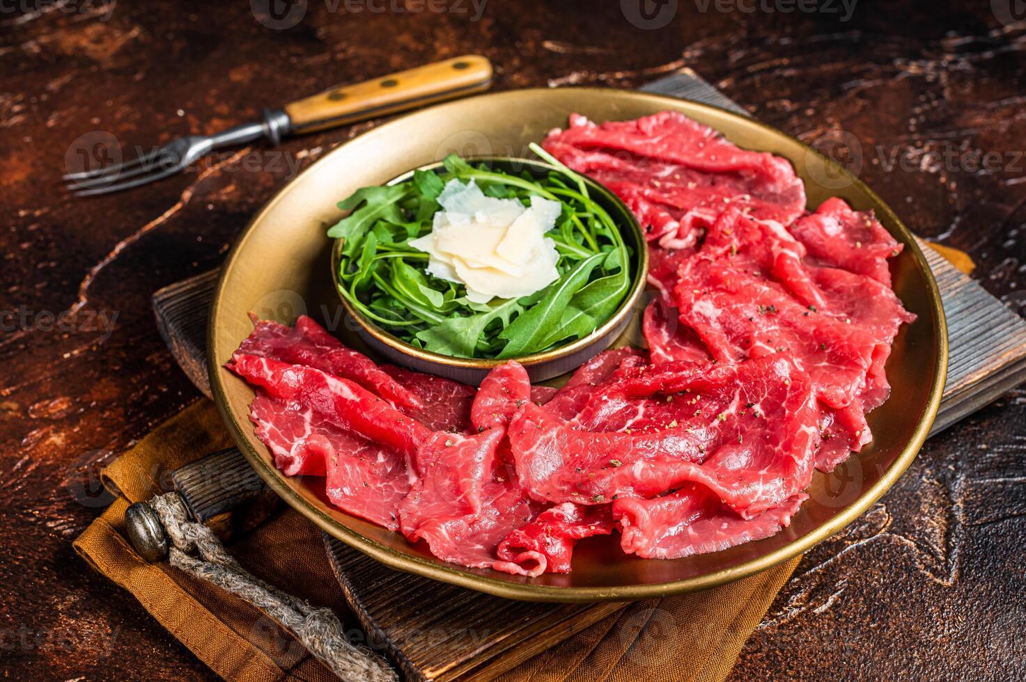 Carpaccio Beef meat appetizer with parmesan and arugula. Dark background. Top view photo