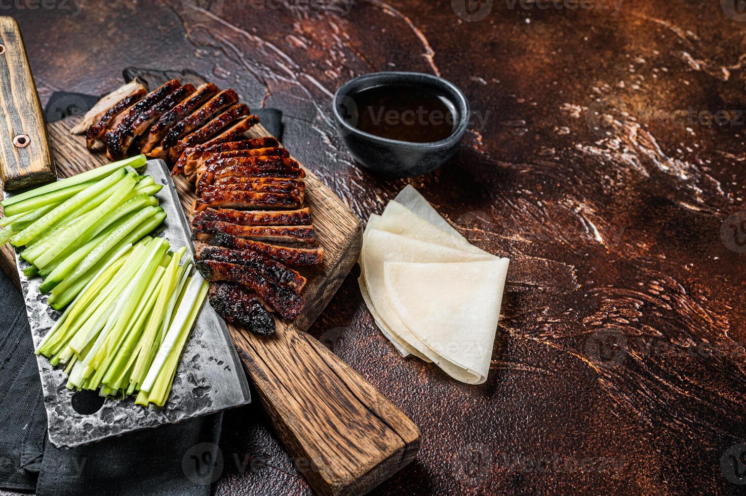 Sliced Peking Duck served with cucumber, green onion, and wheaten chinese pancakes on a meat cleaver. Dark background. Top view. Copy space photo