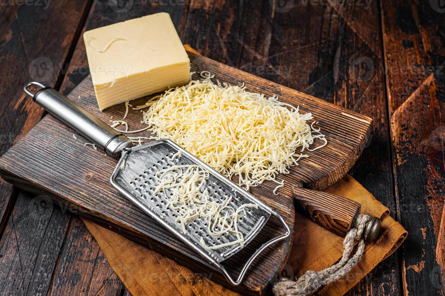 Piece of semi hard cheese and grated cheese with grater. Wooden background. Top view photo