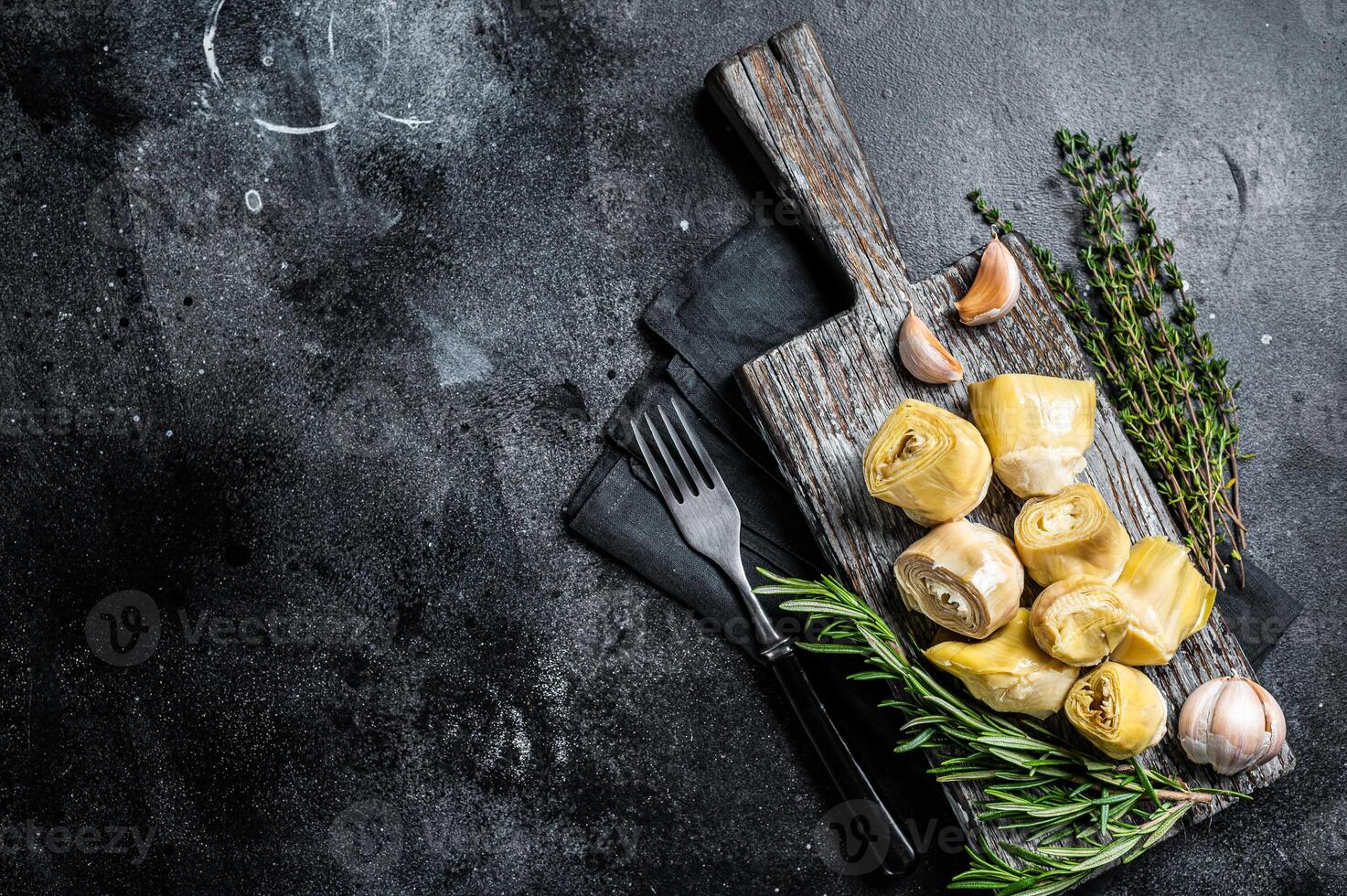 Artichokes hearts marinated with olive oil and herbs, pickled artichoke with garlic on wooden board. Black background. Top view. Copy space photo