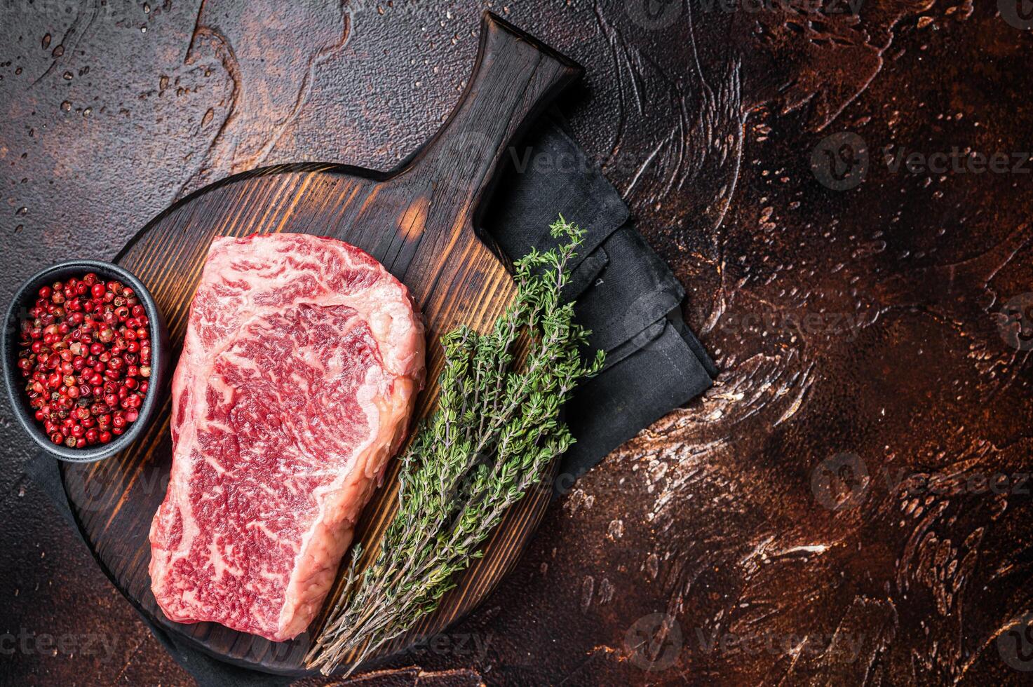 Uncooked Raw striploin or club steak on wooden board with thyme. Dark background. Top view. Copy space photo