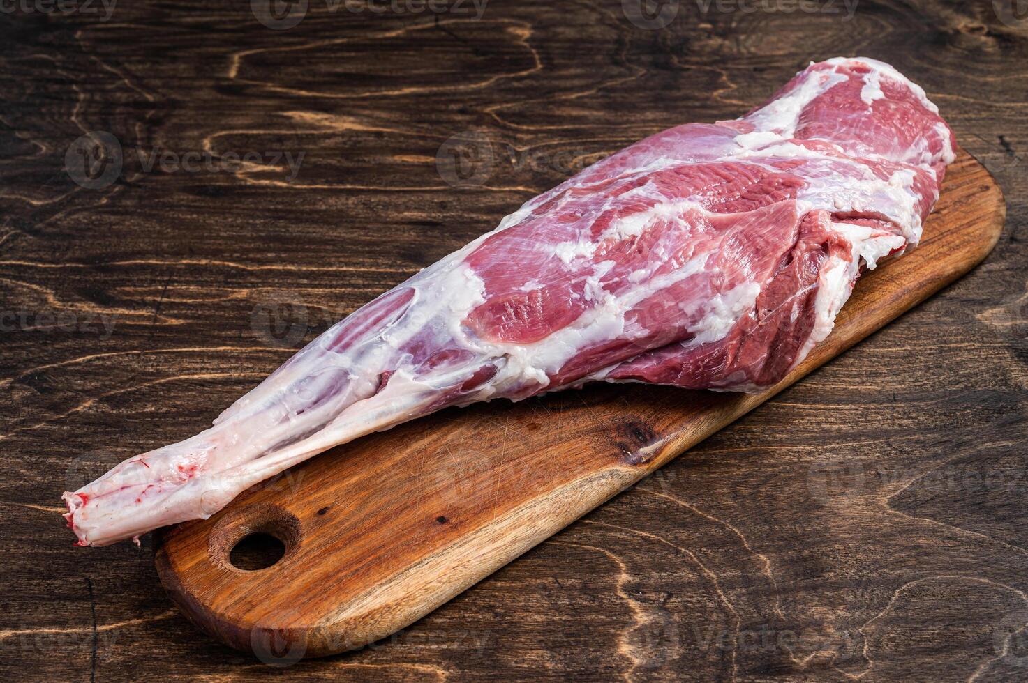 Mutton meat. Raw whole lamb leg thigh on butcher board. Wooden background. Top view photo