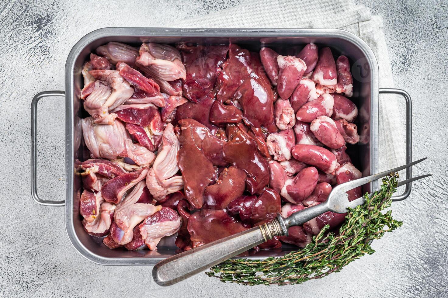 Raw chicken offals meat set, gizzards, stomachs, liver and hearts in a steel tray with herbs. White background. Top view photo