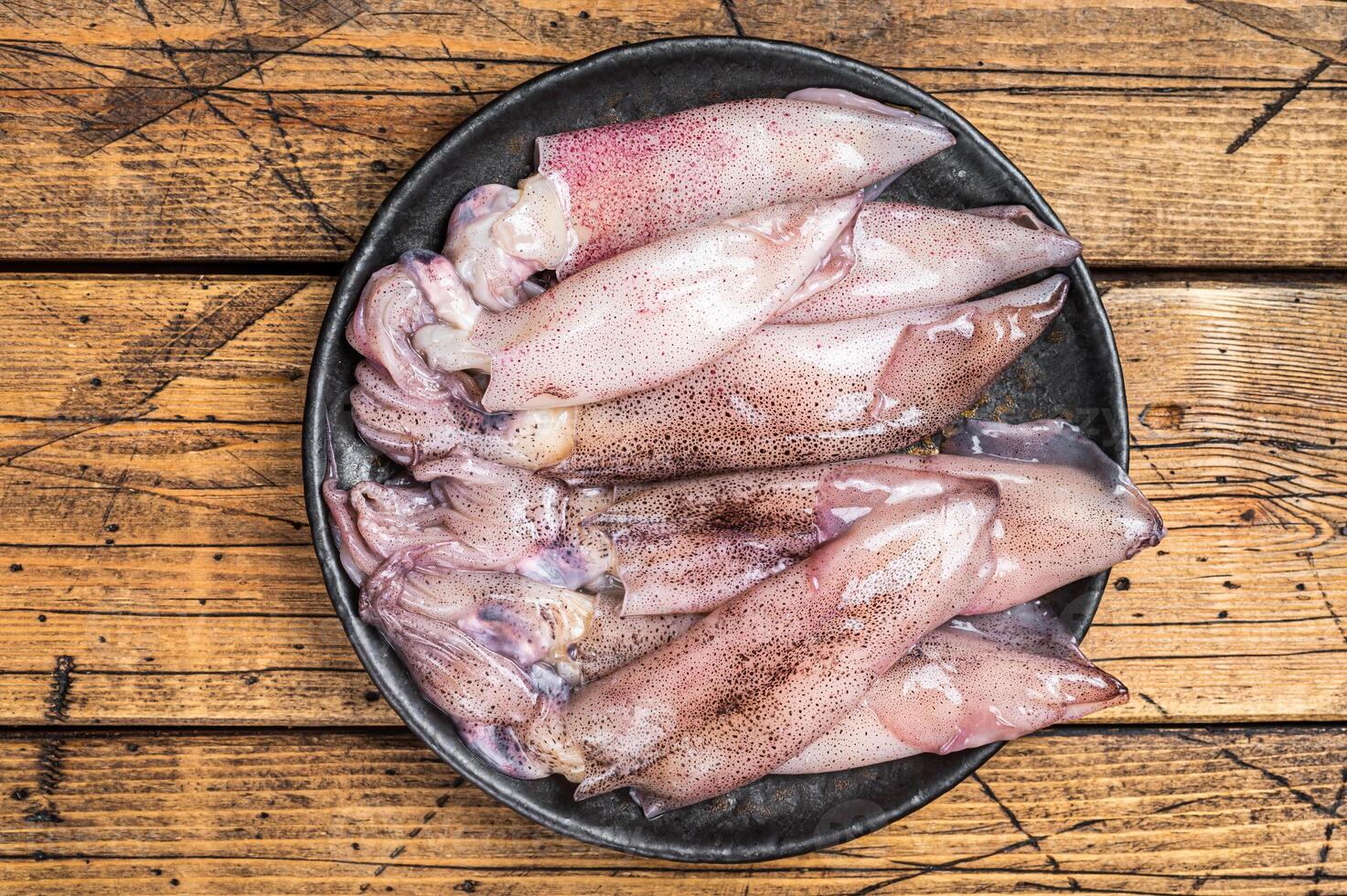Raw squid, fresh calamari in a plate. Wooden background. Top view photo