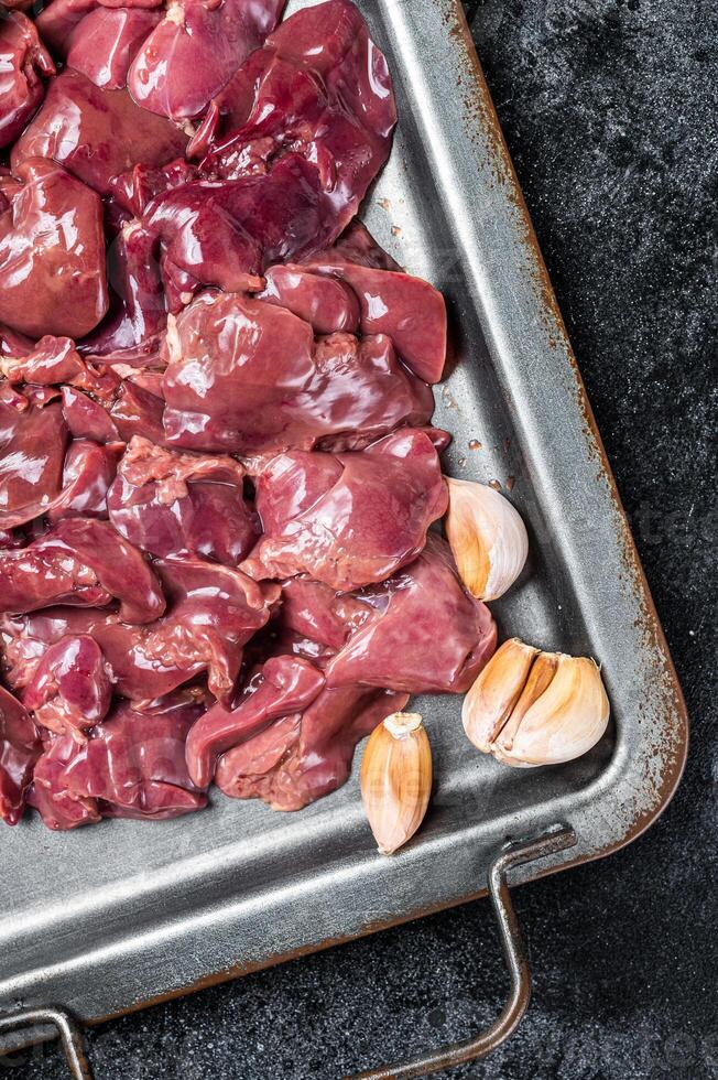 Raw chicken liver meat in steel tray with spices. Black background. Top view photo