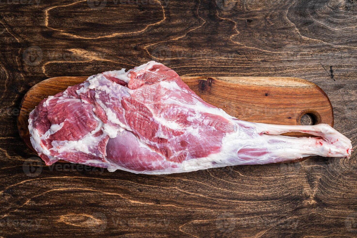 Mutton meat. Raw whole lamb leg thigh on butcher board. Wooden background. Top view photo