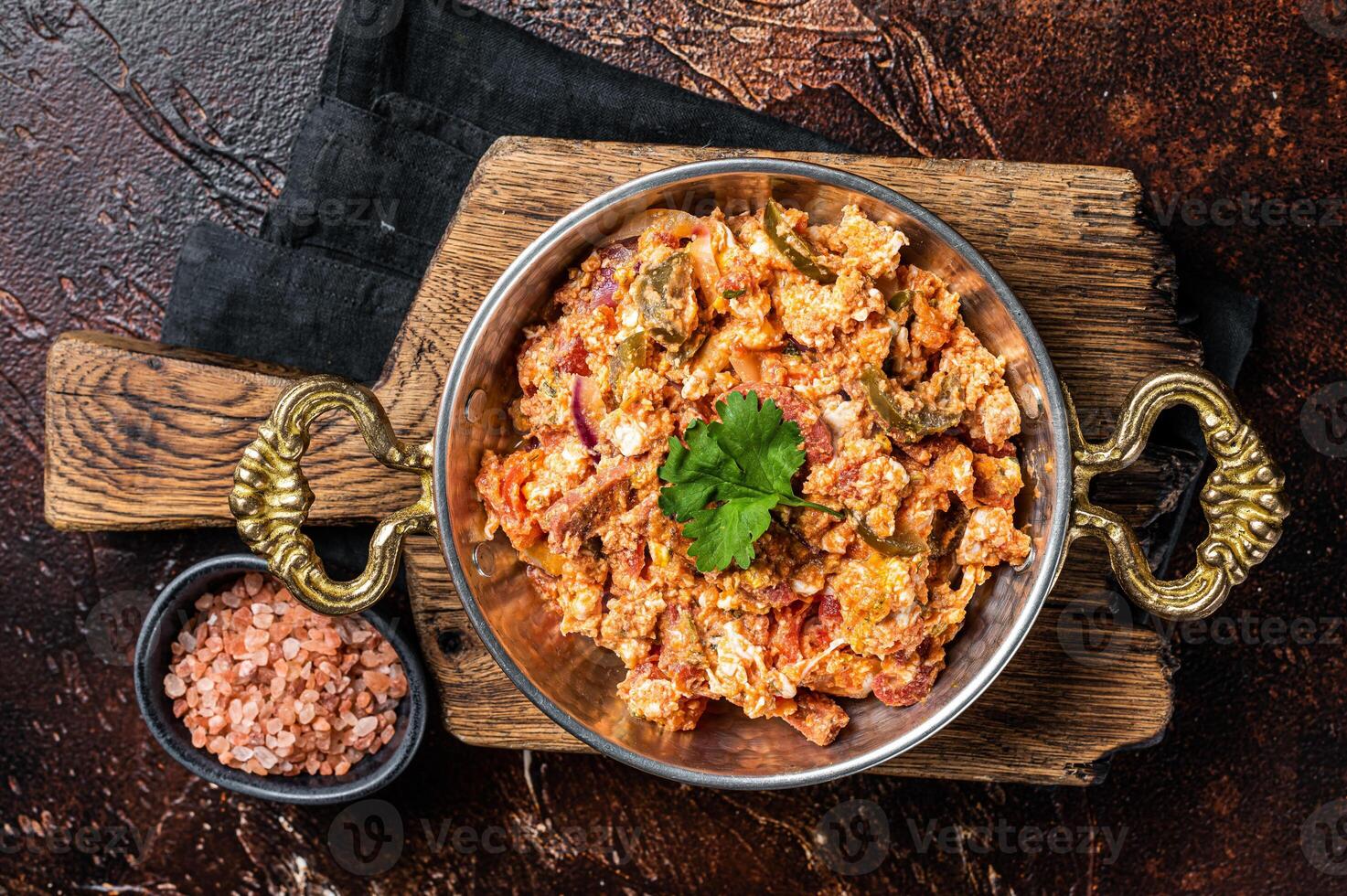 Turkish Menemen omelet with vegetabls and sucuk in askillet. Dark background. Top view photo