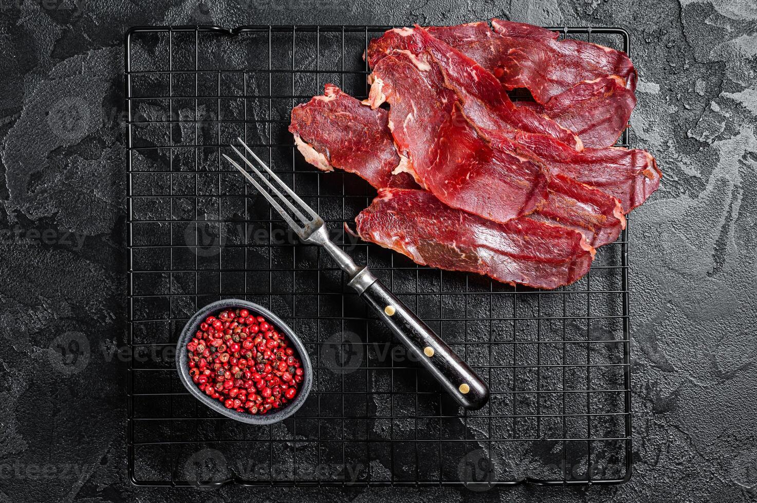 Dried sliced basturma, cured beef meat ready for eat. Black background. Top view photo