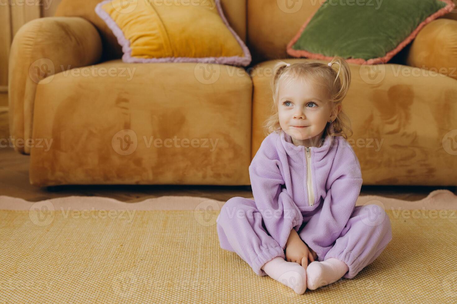 Smiling toddler wearing purple jumpsuit sitting on carpet in living room photo