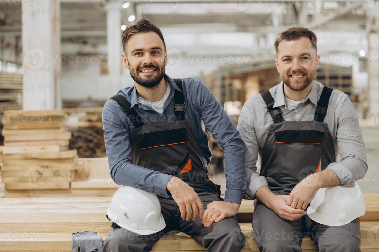 Construction workers smiling and sitting on wood planks in factory photo