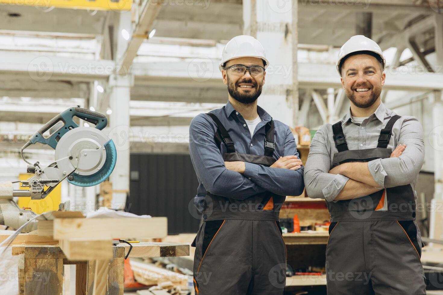 Two smiling carpenters posing with arms crossed in their workshop photo