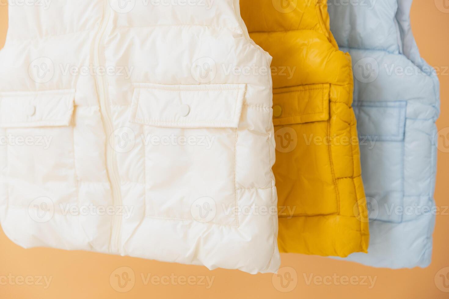 Stylish padded sleeveless jackets hanging on orange background photo