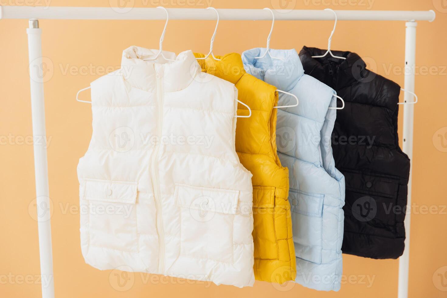 Four sleeveless jackets hanging on clothes rack displaying different colors photo