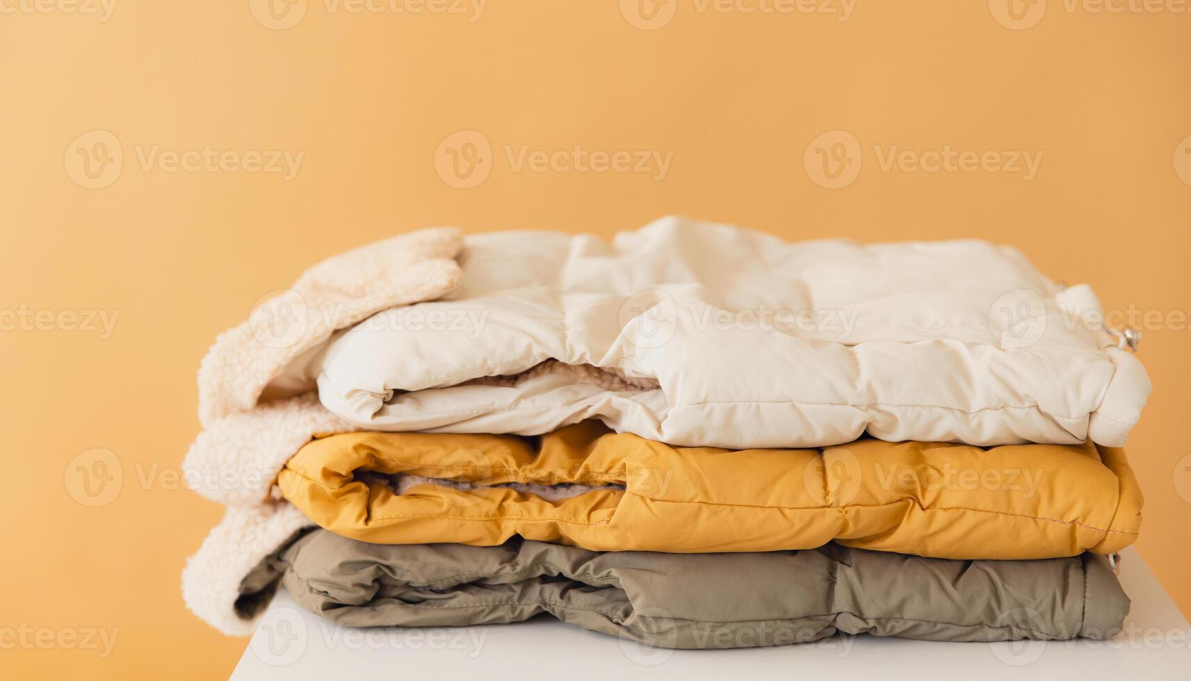 Warm winter jackets folded on table against orange background photo