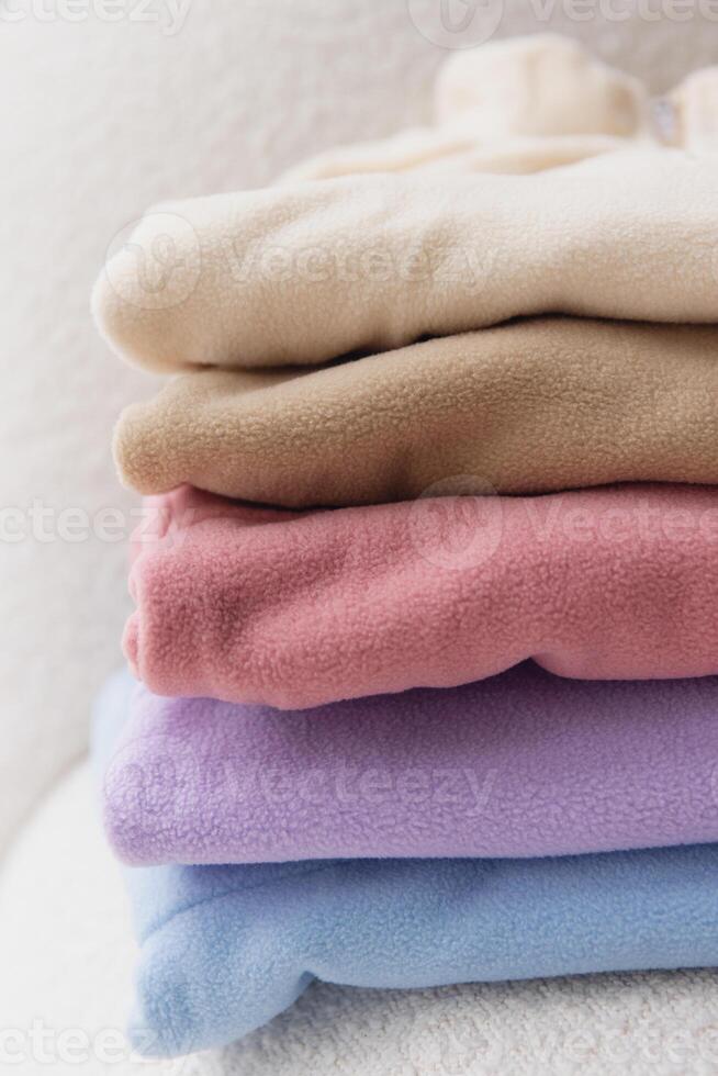 Stack of pastel colored fleece jackets mockup on white sofa photo