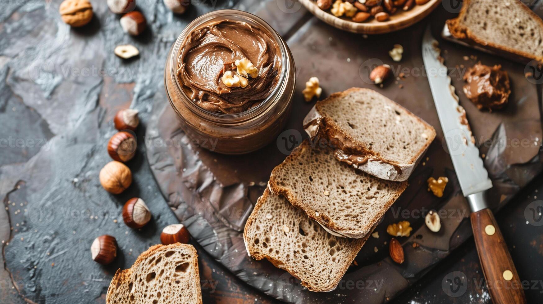 Open jar of hazelnut spread next to sliced loaf of bread and knife, meal photography photo