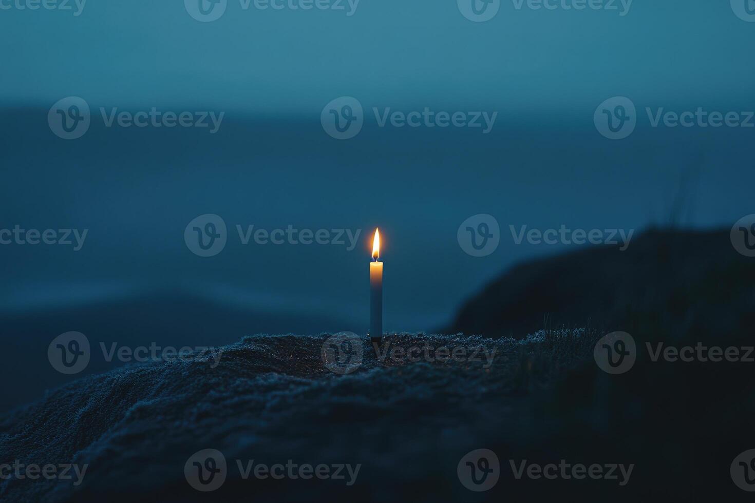 A Single Candle Burning Brightly on a Rocky Outcrop at Dusk photo