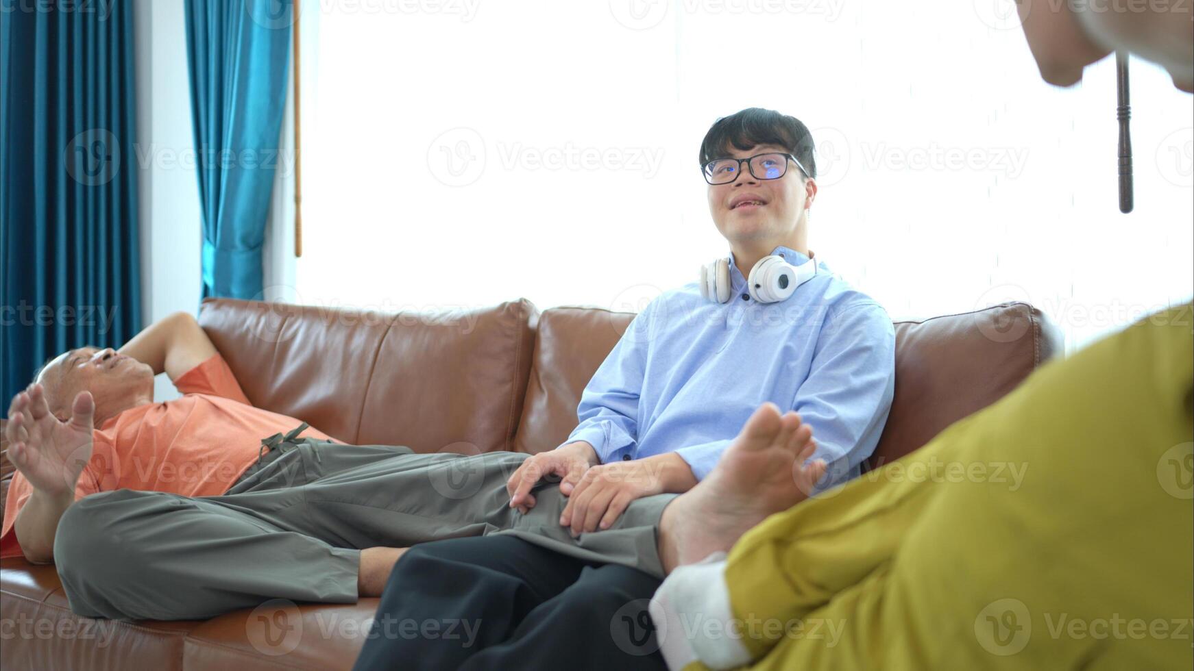 Grandson is massaging his grandfather's legs to relax him in the living room of the house photo