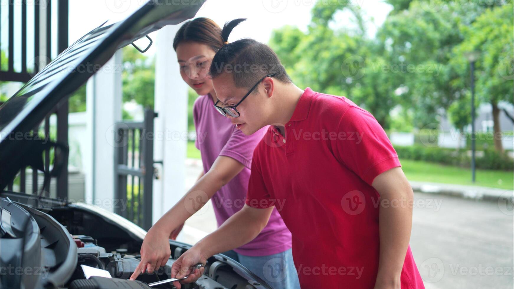 A brother and sister help each other execute a basic engine check on their parents' automobile photo