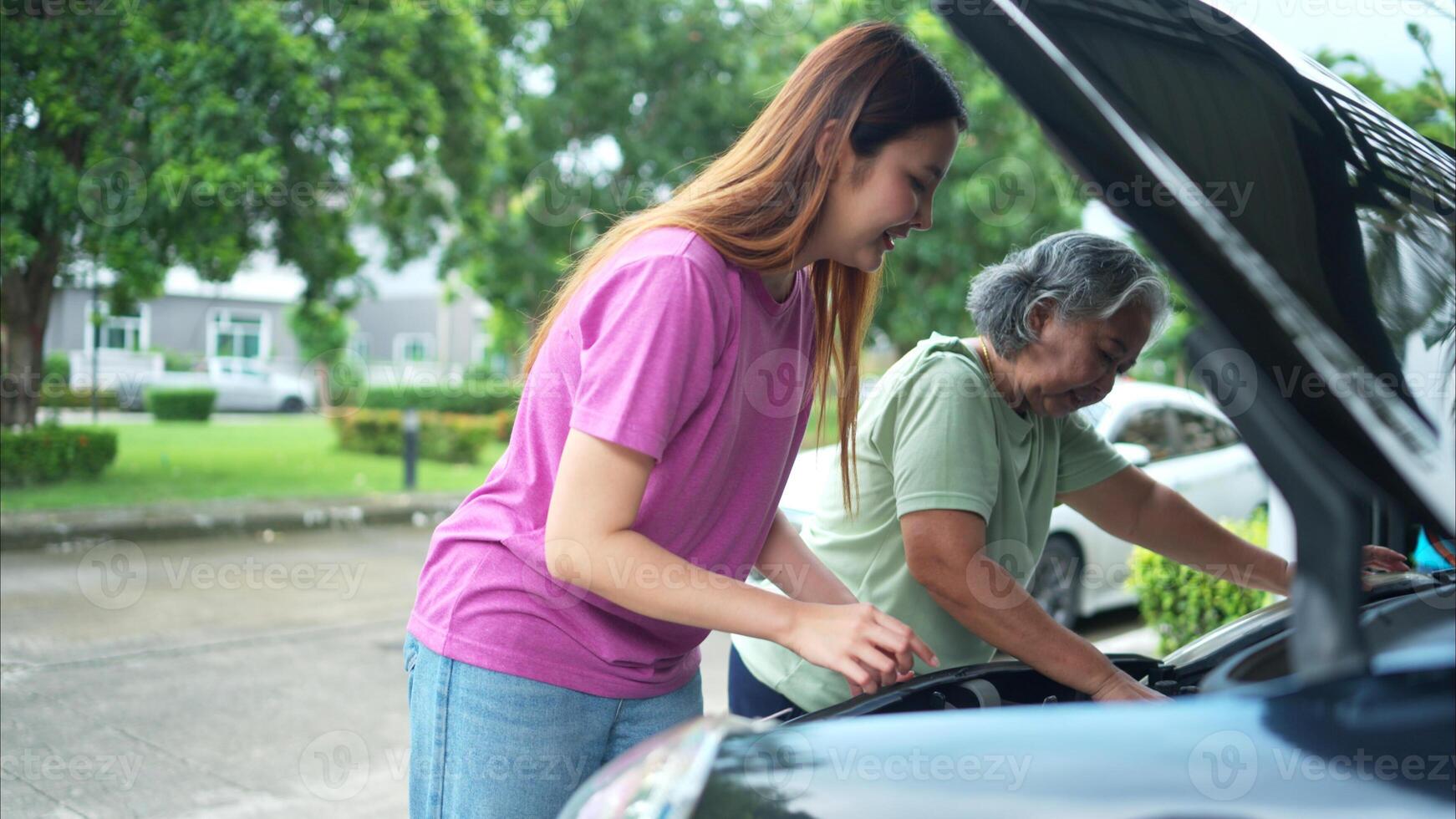 Grandmother and grandchild help each other execute a basic engine check on their parents' automobile photo