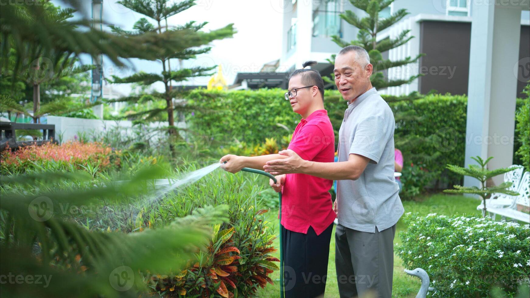 On their day off, the grandfather and grandson help water the trees in the garden of the house photo