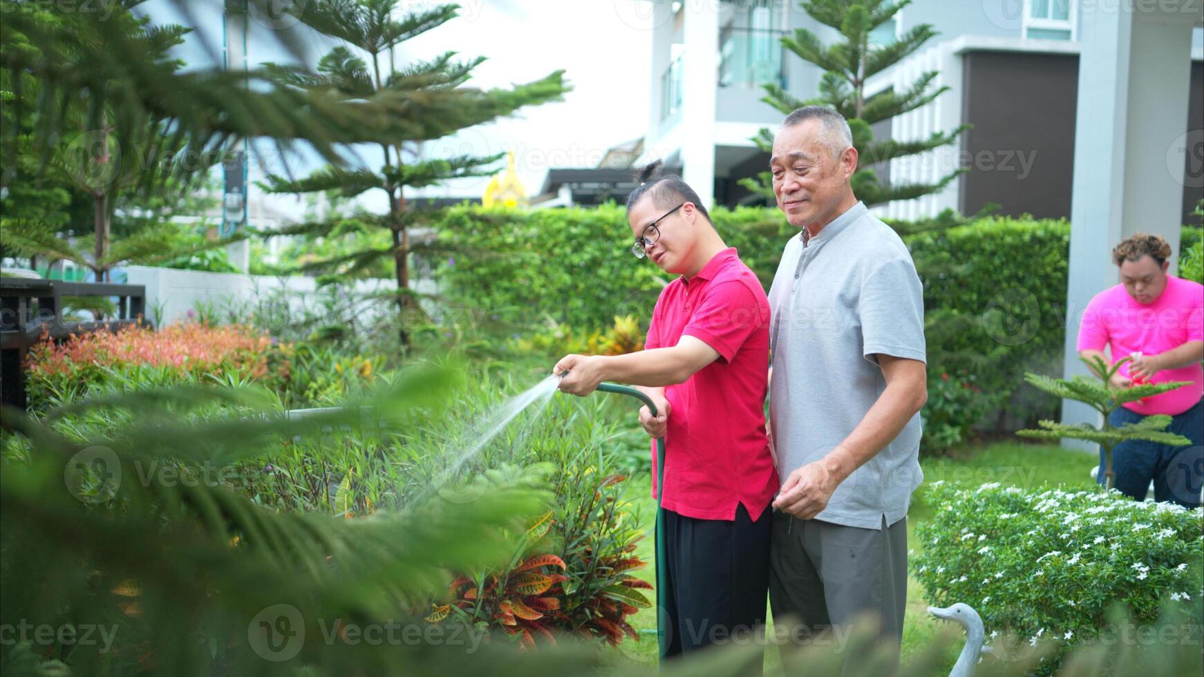On their day off, the grandfather and grandson help water the trees in the garden of the house photo