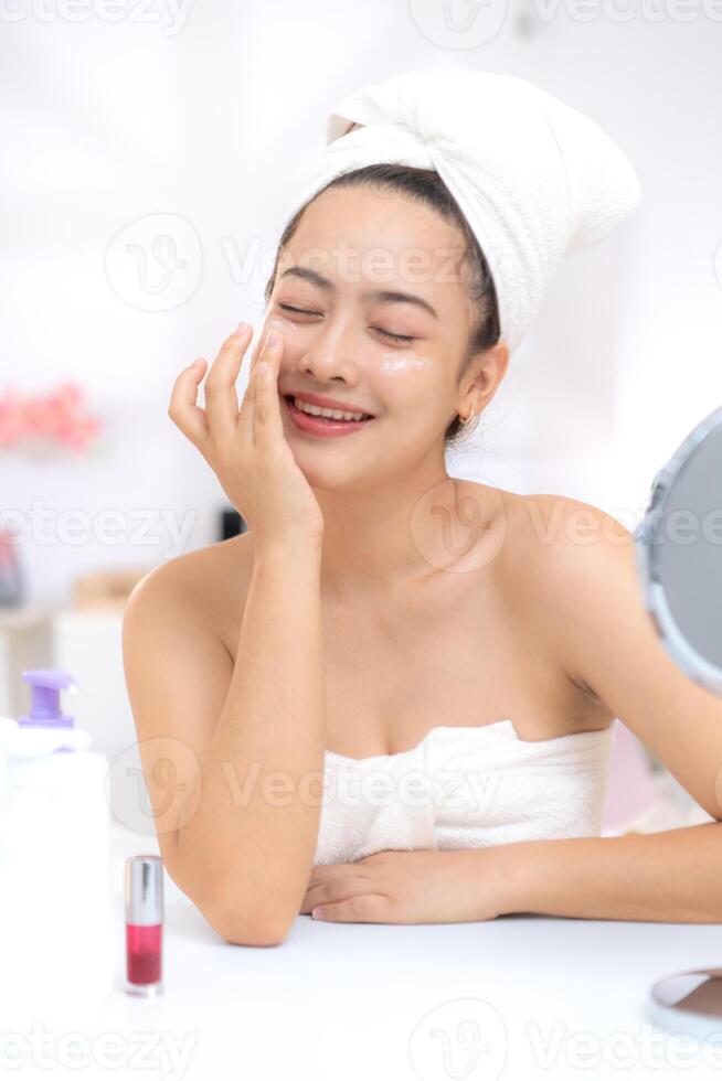 Asian young woman with towel wrapped on head and body applying makeup after shower, Morning beauty routine before work photo