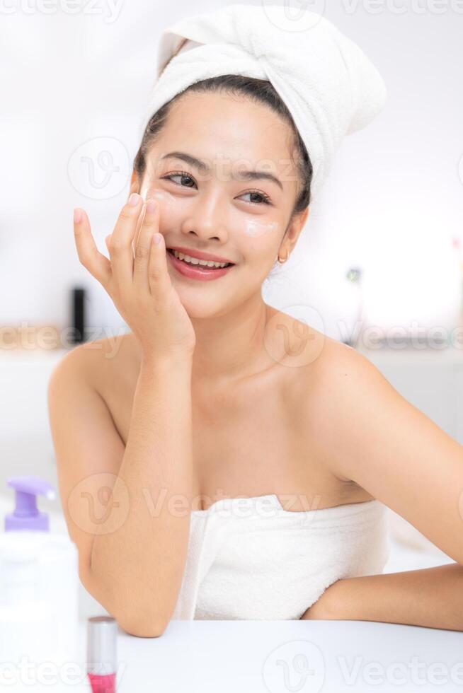 Asian young woman with towel wrapped on head and body applying makeup after shower, Morning beauty routine before work photo
