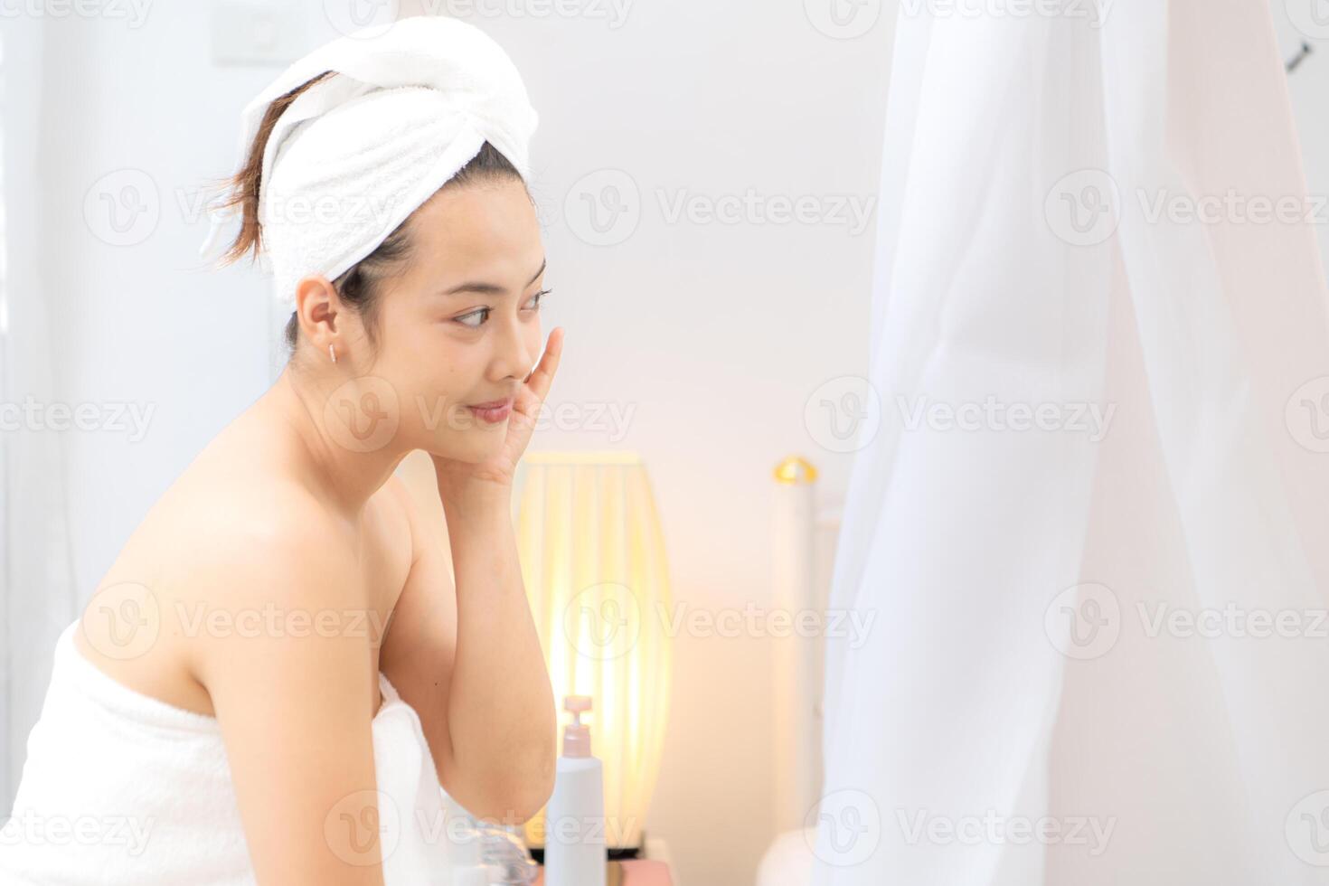 Asian young woman with towel wrapped on head and body applying makeup after shower, Morning beauty routine before work photo