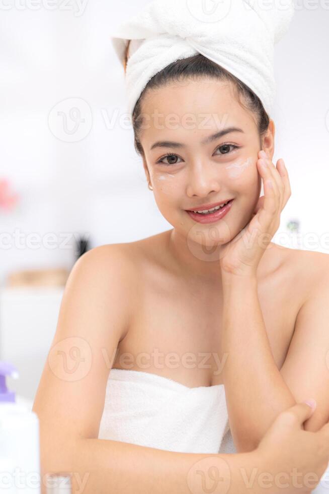 Asian young woman with towel wrapped on head and body applying makeup after shower, Morning beauty routine before work photo